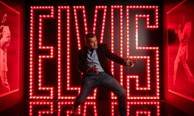 man poses in front of big elvis letters