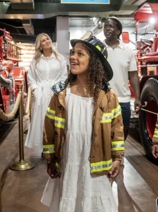 girl at fire museum with parents dressed as firefighter