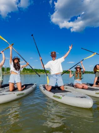 young adults on paddle boards smile for photo while holding up paddles