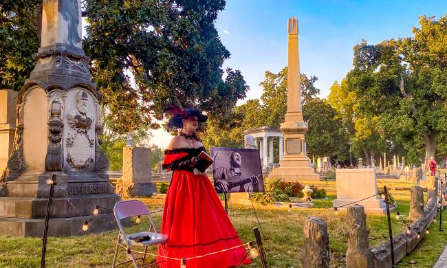 A storyteller dressed in period garb telling stories on a tour of Elmwood Cemetery.